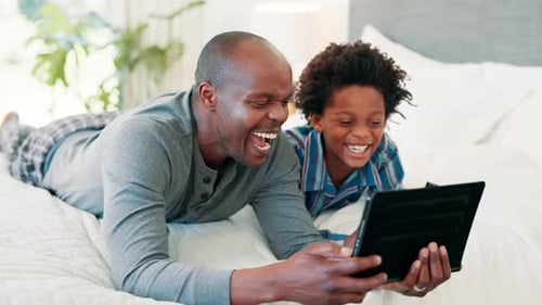 Man and Child Laughing While Using Tablet on Bed