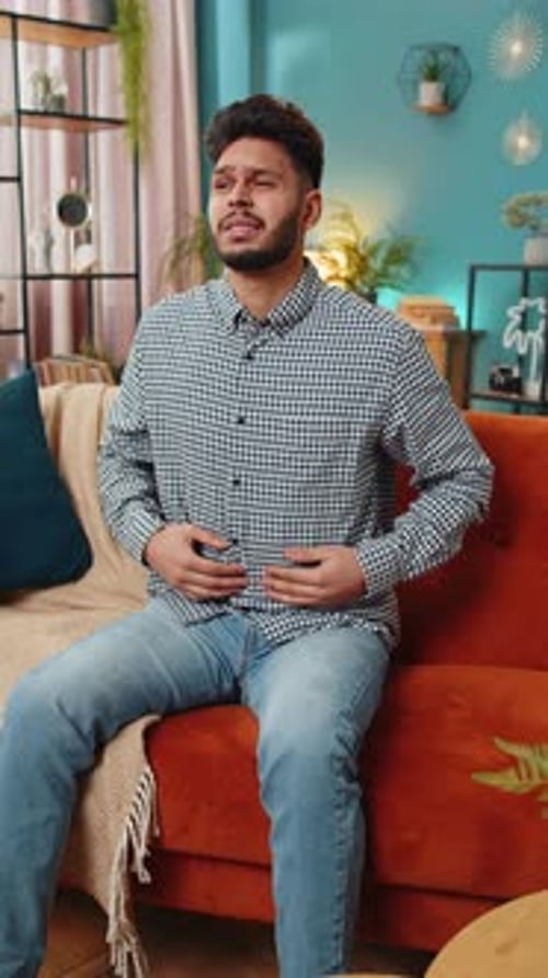 Arabischer Mann sitzt auf dem Sofa und hat plötzliche starke Bauchschmerzen, Gastritis-Problem, Durchfall
