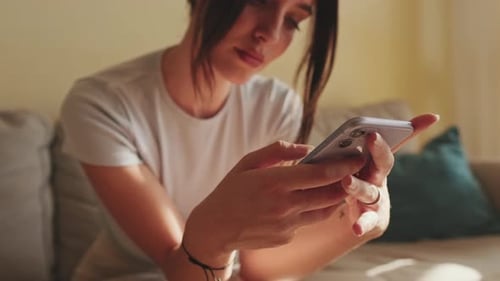 Close-up of young woman's hands using mobile phone while sitting on sofa at home