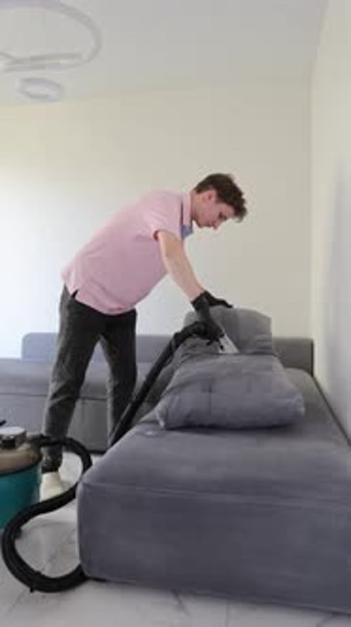 Young man cleaning sofa with professional vacuum cleaner