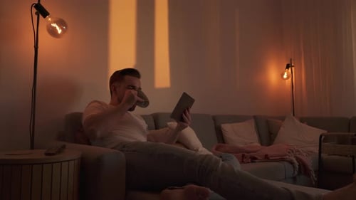 Relaxed man reading tablet with coffee on sofa