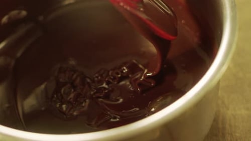 Slow motion liquid chocolate stream mixing in metal bowl preparation