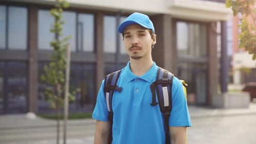 Portrait of the Happy Caucasian Male Courier Standing Near the Office Building Looking at Camera