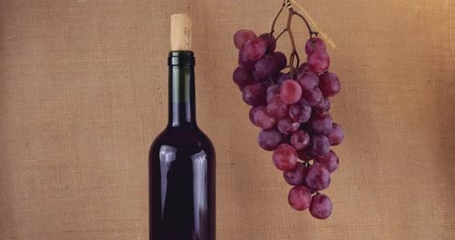 Pink grapes and bottle of wine on a burlap background.