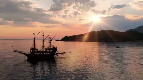 A dramatic pirate ship sailing at sunset near a mountainous coastal island