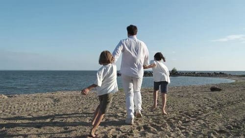 A Father and Two Sons Run Along the Seashore Holding Hands