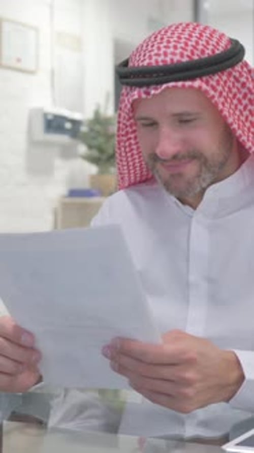 Man Wearing Keffiyeh Reads Documents in Office
