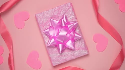Top view of Valentines day decor, pink gift box, heart and ribbon on pastel pink background