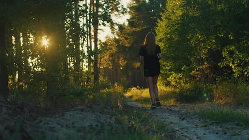 Slow motion female jogger in sportswear running in the forest among green trees, concept of fitness