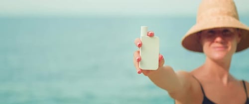 Mujer en traje de baño en la playa sosteniendo un tubo blanco de crema de protección solar para el cuidado de la piel sobre el fondo del océano. Niña