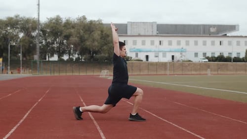 Caucasian Man in Black Shorts and a Tshirt Stretches His Legs and Back at the Stadium Before Running