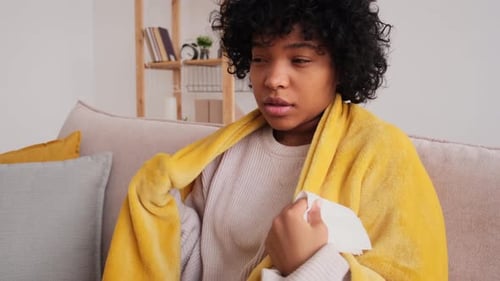 Jeune femme afro-américaine malade malheureuse avec du froid assise sur un canapé à la maison