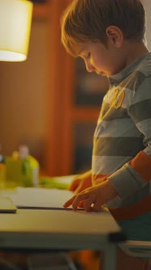 Child Draws on Paper While Standing at a Table in