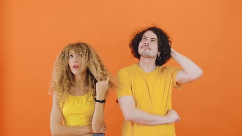 A Curlyhaired Couple a Young Man and Woman are Standing with Their Hands on Their Chins Looking