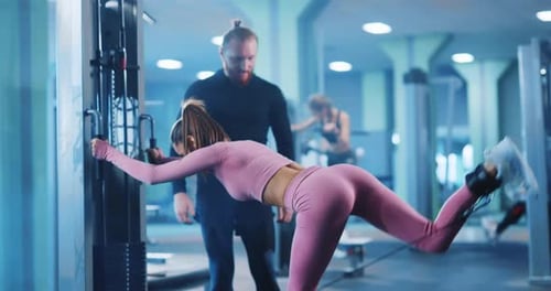 Woman Bodybuilder Doing Strong Leg Exercises with Gym Equipment Under Trainer Supervision