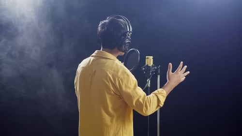 Back View Of A Young Boy With Headphone Singing Into A Condenser Microphone On Black Background