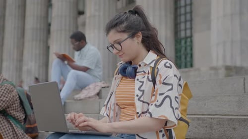 Female Student Using Laptop on Stairs Outside of University