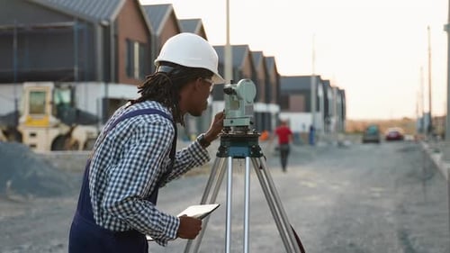 African American Surveyor Engineer Measuring Land with Theodolite in a Modern Cottage Town
