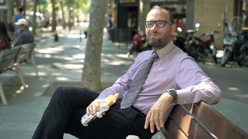 Young businessman enjoying a sandwich break on a bench in the city outdoors