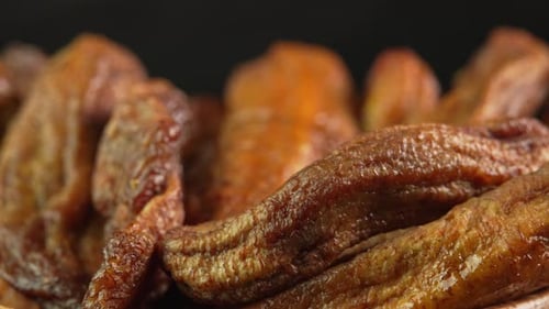 Small dried bananas spinning on black background close up. Sweet dried fruits made from dehydrated