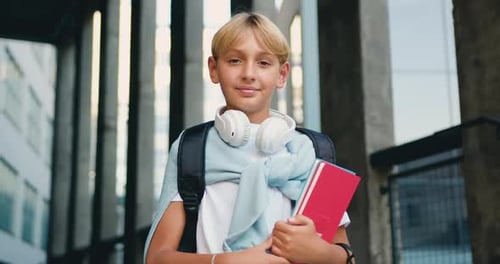 Portrait teen boy standing outside near school looking at camera and smiling. Joyful boy