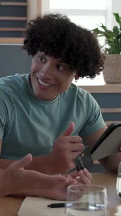 Vertical video: Male student receiving suggestion tilting tablet tapping screen at study table