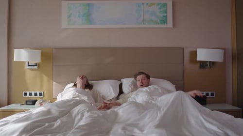 Jeune couple se réveillant brusquement dans un lit d'hôtel avec des expressions choquées se réveillant tard assis