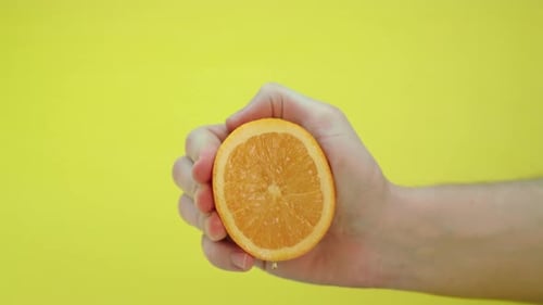 Fresh orange squeezed by a man, causing the juice to fly to the camera lens, slow motion footage.