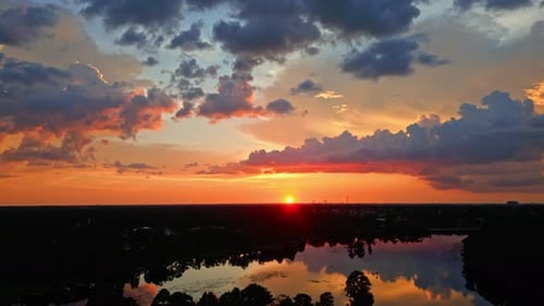 Brillante orange und rote Sonnenuntergangsfarben malen den Himmel über stilles Wasser und Waldrand, himmlisch