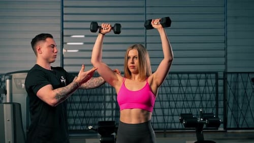 in the Gym Pair Training of a Guy Trainer and a Girl the Guy Controls the Work with Dumbbells