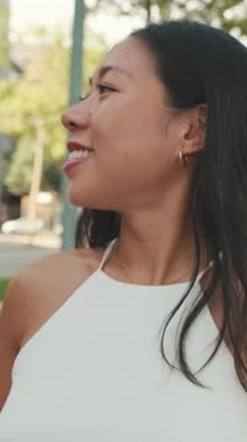 Smiling young woman walking down the street with mobile phone in her hands