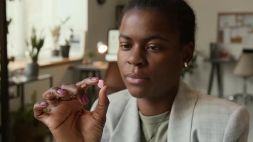Young Woman Examining Round Pill and Taking It with Water in Office Setting