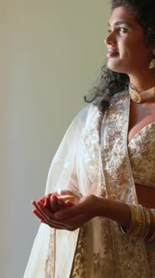 Vídeo vertical: Contemplando uma mulher flamejante segurando diya na cintura no quarto, usando sari dourado, espaço de cópia