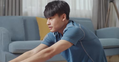 Close Up Of Young Asian Athletic Male In Sports Clothes Doing Hamstring Stretch At Home