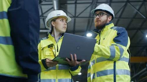 Male and Female Industrial Engineers Talk with Factory Worker while Using Laptop. They Work at the
