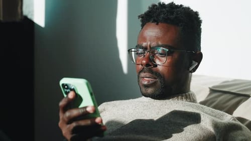 Man in Glasses Looks at Phone Indoors