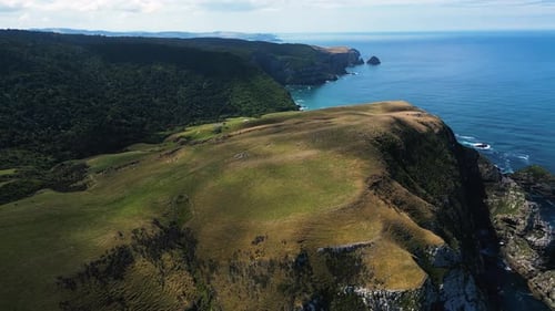 Rotierende Luftaufnahme eines großen unebenen Berggipfels an der Küste des Strandes von Parakanui