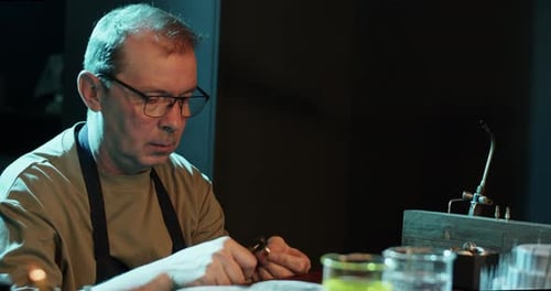 Concentrated Male Goldsmith Making Ring in Dark Workshop