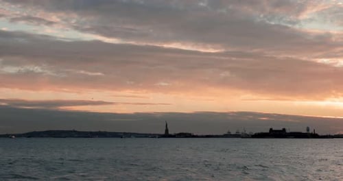 Wide shot of Hudson River upper bay with Statue of Liberty and Ellis Island silhouetted against the