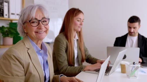 Senior Businesswoman Smiling at Camera Sitting with Colleagues in the Office