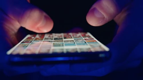 Fingers Scrolling Images on Phone at Night