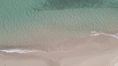 Blick von oben nach unten: weißer Sandstrand aus der Luft mit klarem Meerwasser und kleinen Wellen