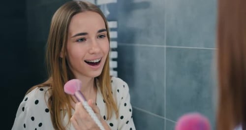 Maquillaje de belleza. Hermosa chica sonriente aplicando cosméticos en la cara con un cepillo frente al espejo