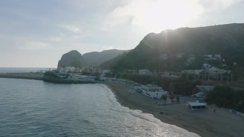 Fly Over Sea Coast Aerial View of Sandy Beach and Buildings in Small Coastal Town Late Afternoon By