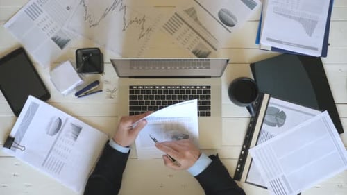 Top View Hands of Young Businessman Looking at Diagrams with Statistic on Paper and Typing Text on