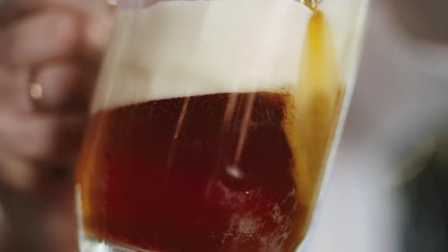 Pouring dark beer with creamy foam into glass