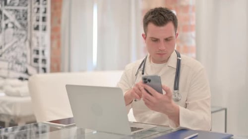 Male Doctor Using Laptop and Smartphone in Clinic