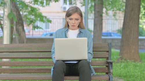 Woman Reacting to Trade Loss on Laptop while Sitting on Bench in Park