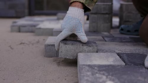 Worker Laying Concrete Paving Block on Sand Base During Installation