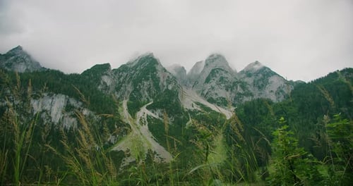 Dramatic mountain peaks covered in greenery and rocky textures stand against a cloudy sky, exuding r